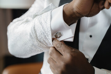 A man in a white suit straightens his sleeves A man buttoning a white jacket with black details Groom getting ready in the morning before the wedding ceremony Groom adjusting his cufflinks Close up 