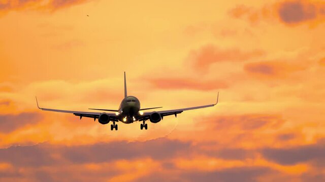 Jet plane flies at beautiful sunset for landing. Airplane silhouette approaching in golden sunset