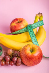 Fresh fruits and measuring tape on a pink background. The concept of diet and healthy eating.