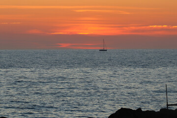 Tramonto di fiamma in Toscana, con sagome di barca e scoglio.
