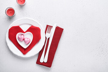 Valentinas day table setting white color with white silverware, red napkin folded as heart, candles, champagne, glasses on white background for greetings. Romantic dinner or menu concept. Mock up.