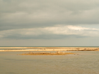 View of a shallow lagoon separated from the sea by a slanting sandy beach in early spring on a sunny day. Yellow shell-sand islands in seawater