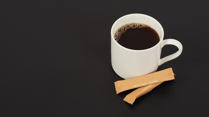 Hot coffee in white mug and two brown sugar sachet isolated on black background.