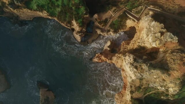 Aerial shot, directly above raging ocean and Ponta da Piedade headland with group of rock formations yellow cliffs along limestone coastline, Lagos town, most famous touristic attractions of Portugal