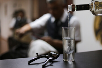 Serving shot of tequila on wooden table next to razor in background barbershop
