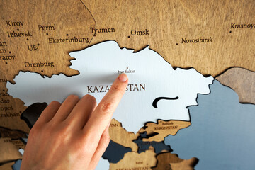 Kazakhstan on wooden world map. Finger points on capital of the country Nursultan.