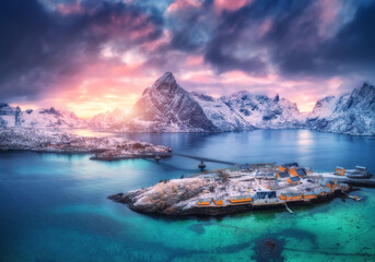 Aerial view of snowy islands with houses, rorbu, blue sea, mountains, bridge and colorful cloudy...