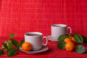 Two cups of coffee with saucers and the tangerines with green leaves on red background. Copy space.	
