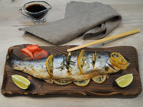 Fried arctic char fish, salmon family, stuffed with lemon and lime, pickled ginger, soy sauce on the kitchen board, top view, flat layout. Recipe for healthy seafood Salvelinus alpinus 