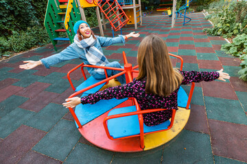 Two childish happy woman friends or teenage girl having fun on seesaw and carousel on a playground....
