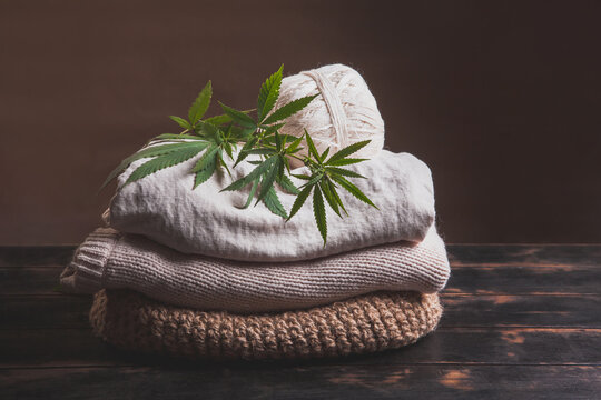 A stack of various types of hemp fiber fabrics. Hemp threads, yarn and fabric with cannabis leaves on a wooden background