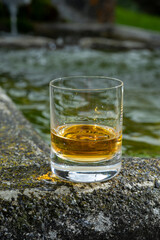 Glass of strong scotch single malt whisky served on old stone reservoir for water from mountain spring