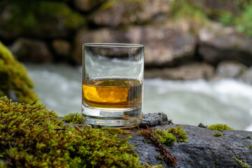 Glass of strong scotch single malt whisky with fast flowing mountain river on background