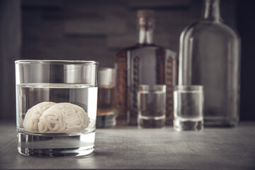 Human brain model in a glass with an alcoholic drink, against the background of bottles with alcohol. Alcohol addiction. Alcohol damage to the brain