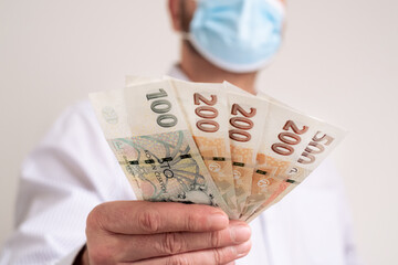 Fan of Cash Czech republic koruna. Finance during coronavirus in Czechia concept. CZK small banknotes. Man in a protective medical face mask holds krona cash.