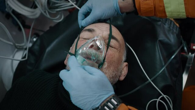 From above anonymous doctors putting oxygen mask on ill aged man while working in ambulance during emergency