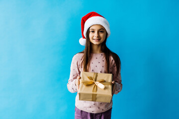 Happy little girl wearing christmas hat with a gift box isolated on blue background.