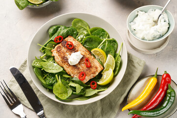 A plate with fresh green raw spinach and fried wild salmon, lime slices, cream cheese sauce, red chilli pepper on grey concrete surface