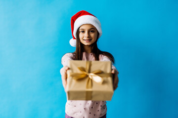 Smiling teenage girl in santa helper hat holding gift box over lights on blue background