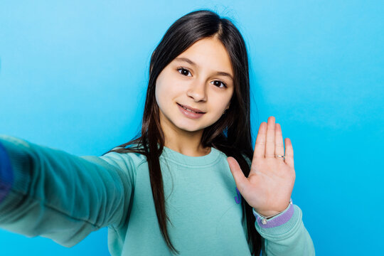 Portrait of happy friendly caucasian little girl over blue background taking selfie wave hello