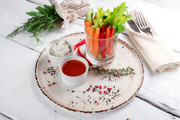 Sticks of fresh vegetables in a glass. Chopped carrot, cucumber, celery, pepper with tomato sauce and zaziki