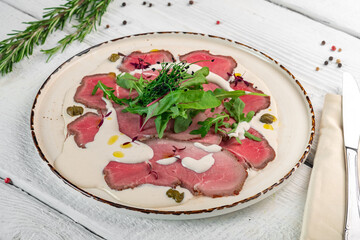 Beef carpaccio with spinach salad and nut sauce. A dish of sliced meat on a white plate