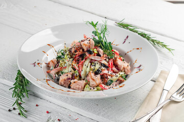 Tuna salad with red pepper, olives, cucumber, sesame and teriyaki sauce. Canned tuna with vegetables on a white plate