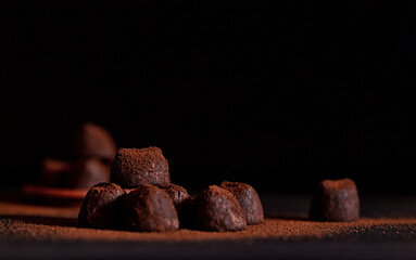 Dark chocolate truffles in scattered cocoa powder close-up. Weak light. Selective focus