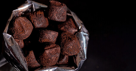 Lots of chocolate truffles in a packing bag on a dark background with an empty space. Selective focus