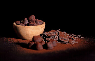 Chocolate truffles covered with cocoa powder in a wooden cup and a slide of milk chocolate on a dark background. Weak light. Selective focus