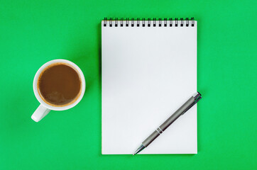 Notepad with white blank pages, pen and cup of coffee on bright green background.