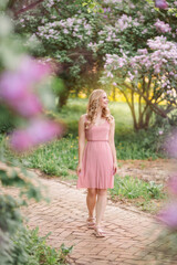 Fototapeta na wymiar a girl in a pink dress walks in the park among the flowering bushes of lilac