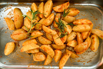 top view of potato slices with spices and rosemary on a metal tray
