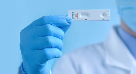 A doctor wearing a protective mask and gloves shows a rapid laboratory test for COVID-19 IHU variant strain to detect IgM and IgG antibodies to the new coronavirus. Copy space