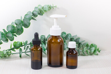 Various glass bottles for cosmetics, essential oils or other liquids on a white background with eucalyptus branch.