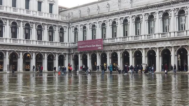 Venice, Italy - January 2022 - San Marco square submerged by high water on a sunny day while tourists are having fun with colored boots