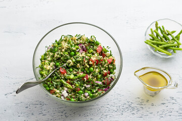 Traditional middle eastern or arabic tabbouleh salad of bulgur, tomatoes, asparagus, green peas and greens on light gray background, top view. Healthy homemade vegan food