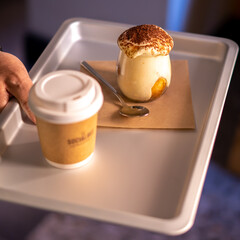 Man holding tray with take away coffee and Tiramisu in glass. coffee flavored Italian dessert made of ladyfingers and mascarpone