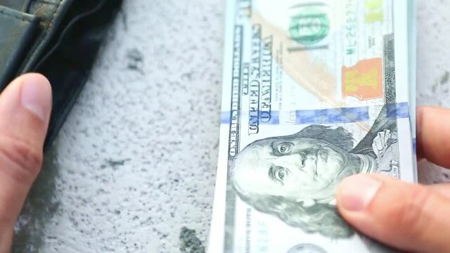Hand puts a hundred-dollar bill in a pile and takes a banknote. Cash money, Stack of $100 bills in close-up. Finance, economy, financial planning, economics, savings.
