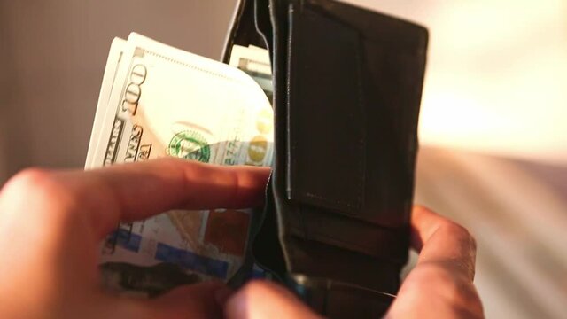 Hand puts a hundred-dollar bill in a pile and takes a banknote. Cash money, Stack of $100 bills in close-up. Finance, economy, financial planning, economics, savings.