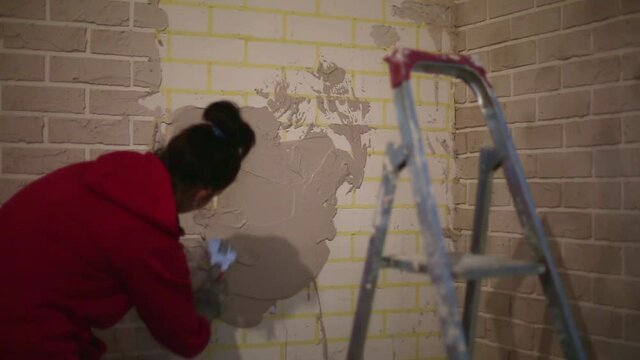 Imitation of stucco brickwork. Home renovation is a DIY made of construction mix and scotch tape. A woman puts mortar on the wall and makes fake bricks