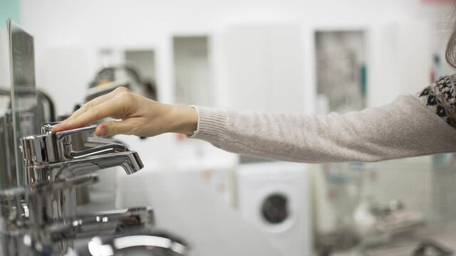 Young woman with brunette curly hair wearing warm printed sweater and jeans chooses new faucet for flat bathroom renovation closeup