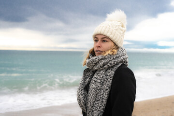 portrait d'une jeune femme blonde avec une écharpe et un bonnet devant l'océan, en hiver