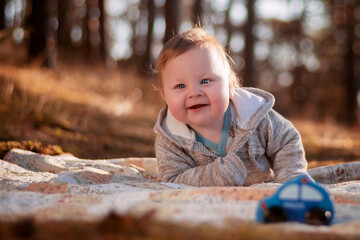 An eight-month-old boy lying on a blanket in the forest.
