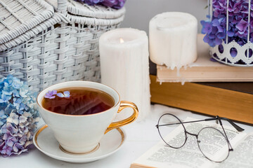A visual for content. Still life in vintage style. A mug with a drink, an old book, a cage, candles and hydrangea flowers in the garden on a white wooden table. The concept of a tea ceremony.