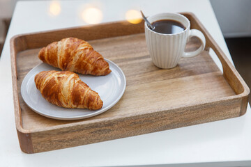 Freshly baked croissant on a gray round plate, white cup with coffee and garland on a tray on the table