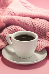 Morning coffee. Cup of coffee with a saucer, knitted scarf on a pink background.