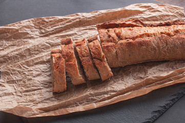 Rustic bread, beautiful golden crust, sliced bread and knife lying on black board