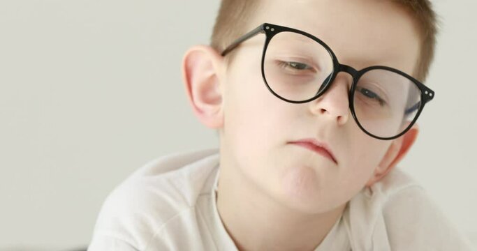 a little boy has a headache, holds his head with his hands. Portrait of caucasian 7 years old boy in glasses. feelings and emotions concept. 4k.