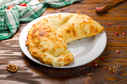 khachapuri in Gurian with cheese and egg inside on white plate on wooden table